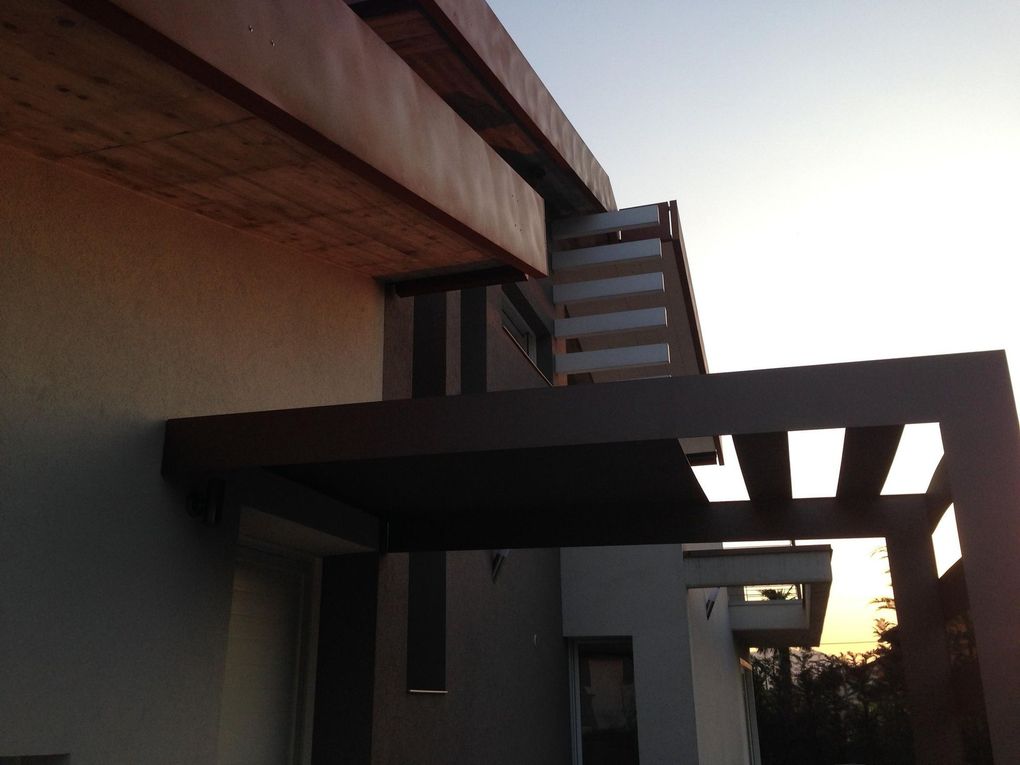 Esterno di una casa moderna con pergolato e balcone al tramonto.