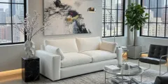 A tan leather sectional sofa with a chaise lounge sits on a grey rug in a modern, well-lit living room.