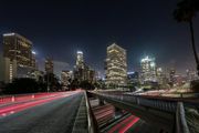 Night view of the Los Angeles skyline with long-exposure light trails from traffic on a highway overpass.