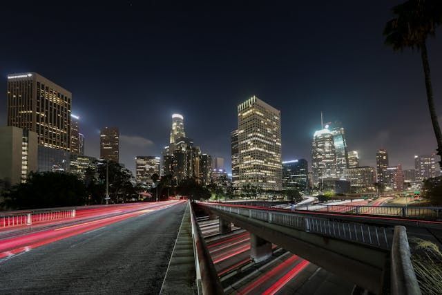 Night view of the Los Angeles skyline with long-exposure light trails from traffic on a highway overpass.