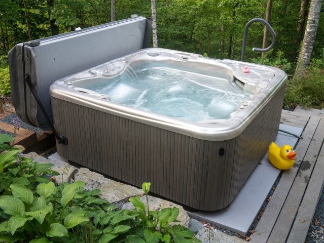 Outdoor hot tub on a wooden deck beside a forest, with a yellow duck toy floating nearby.