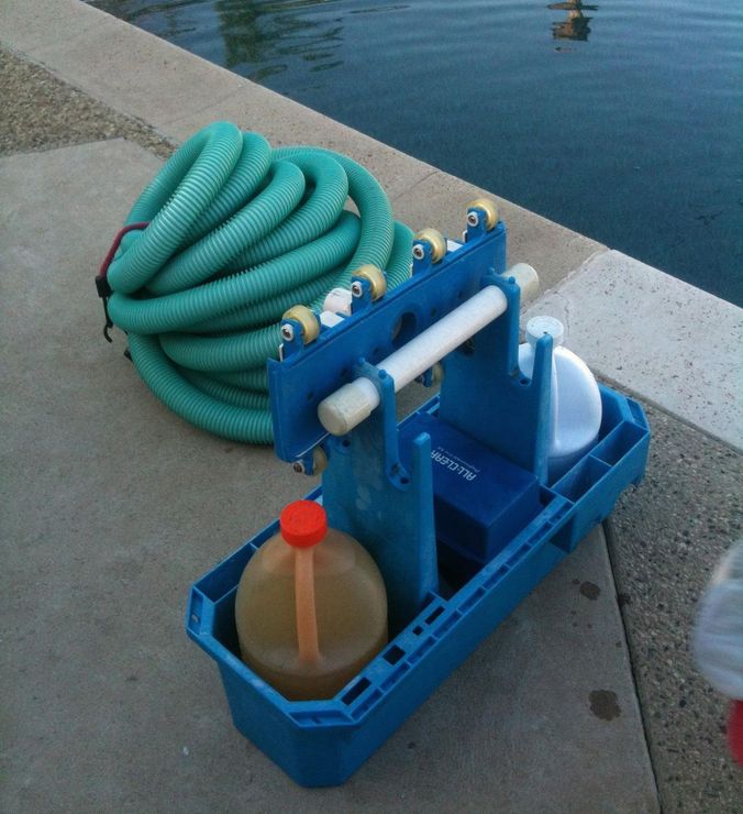 Blue poolside cleaning caddy with coiled green hose and bottle beside the water