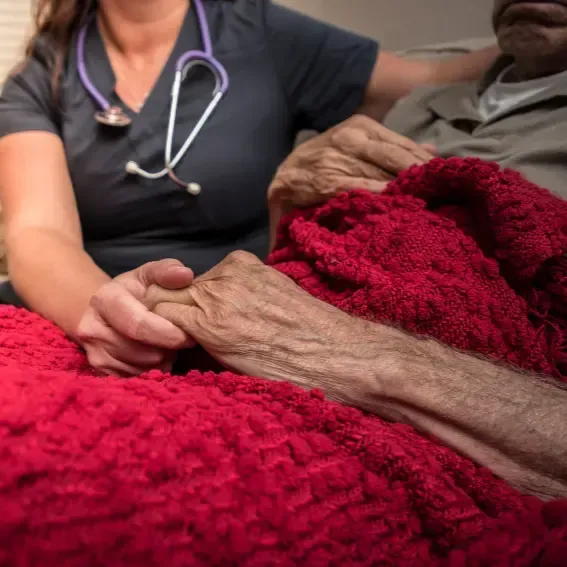 A nurse is holding the hand of an elderly man.