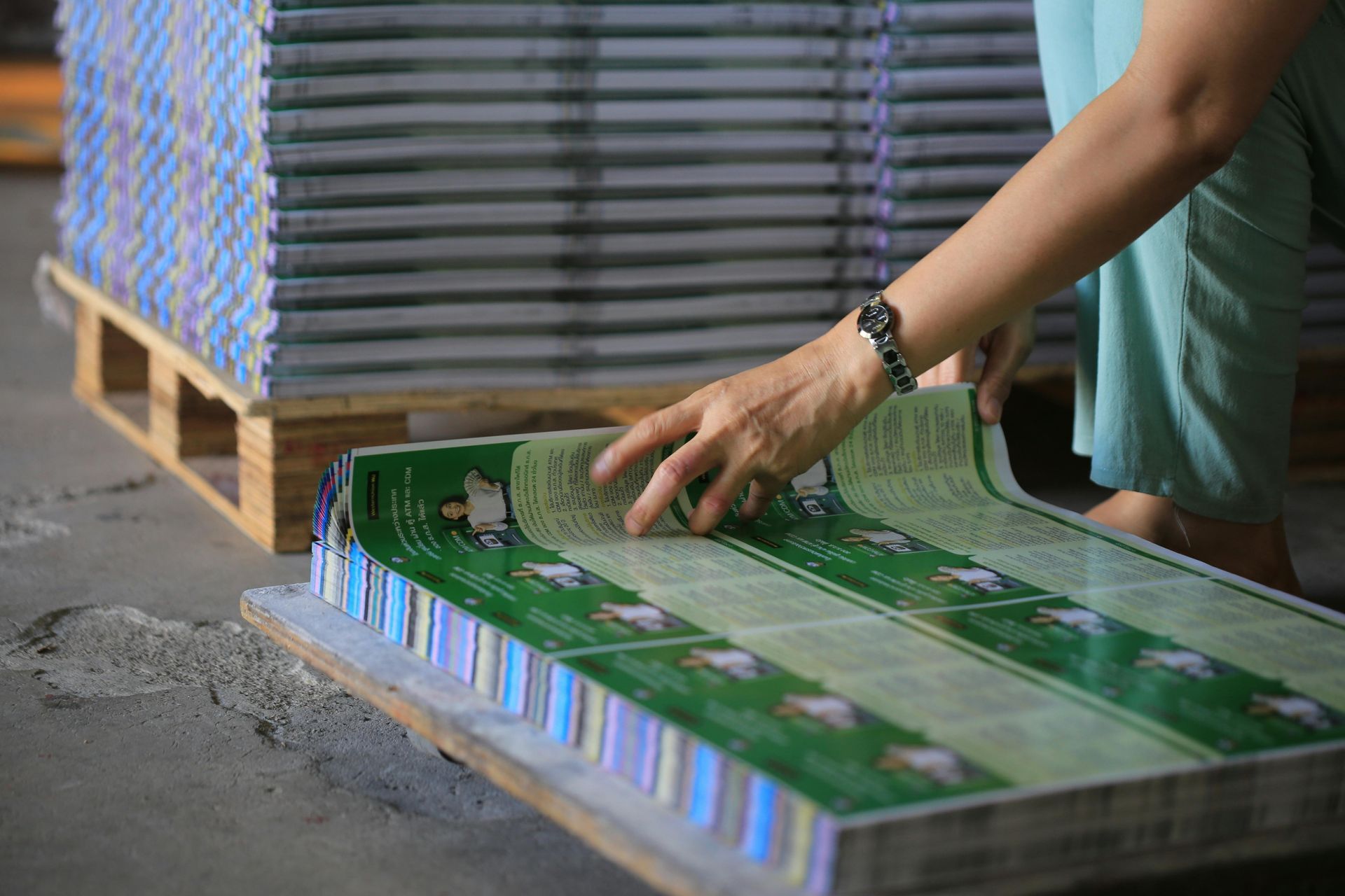 Woman arranging printed pages on a pallet near a stack of books in a factory.