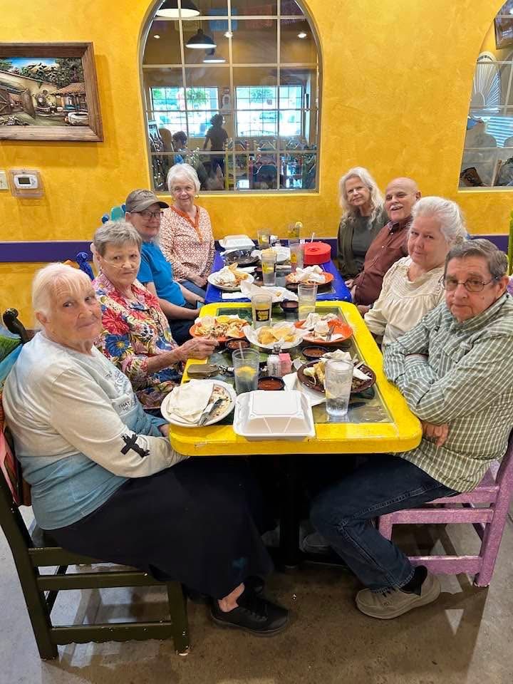 Group seated around a yellow restaurant table, sharing a meal in a bright café with yellow walls.