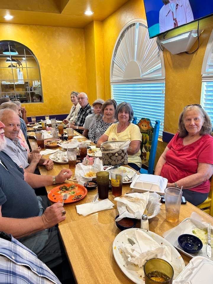Group of people dining together at a restaurant table with plates, drinks, and yellow walls.