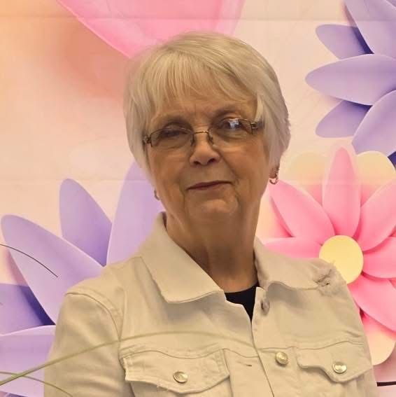 lady with silver hair standing in front of a wall with pink and purple flowers