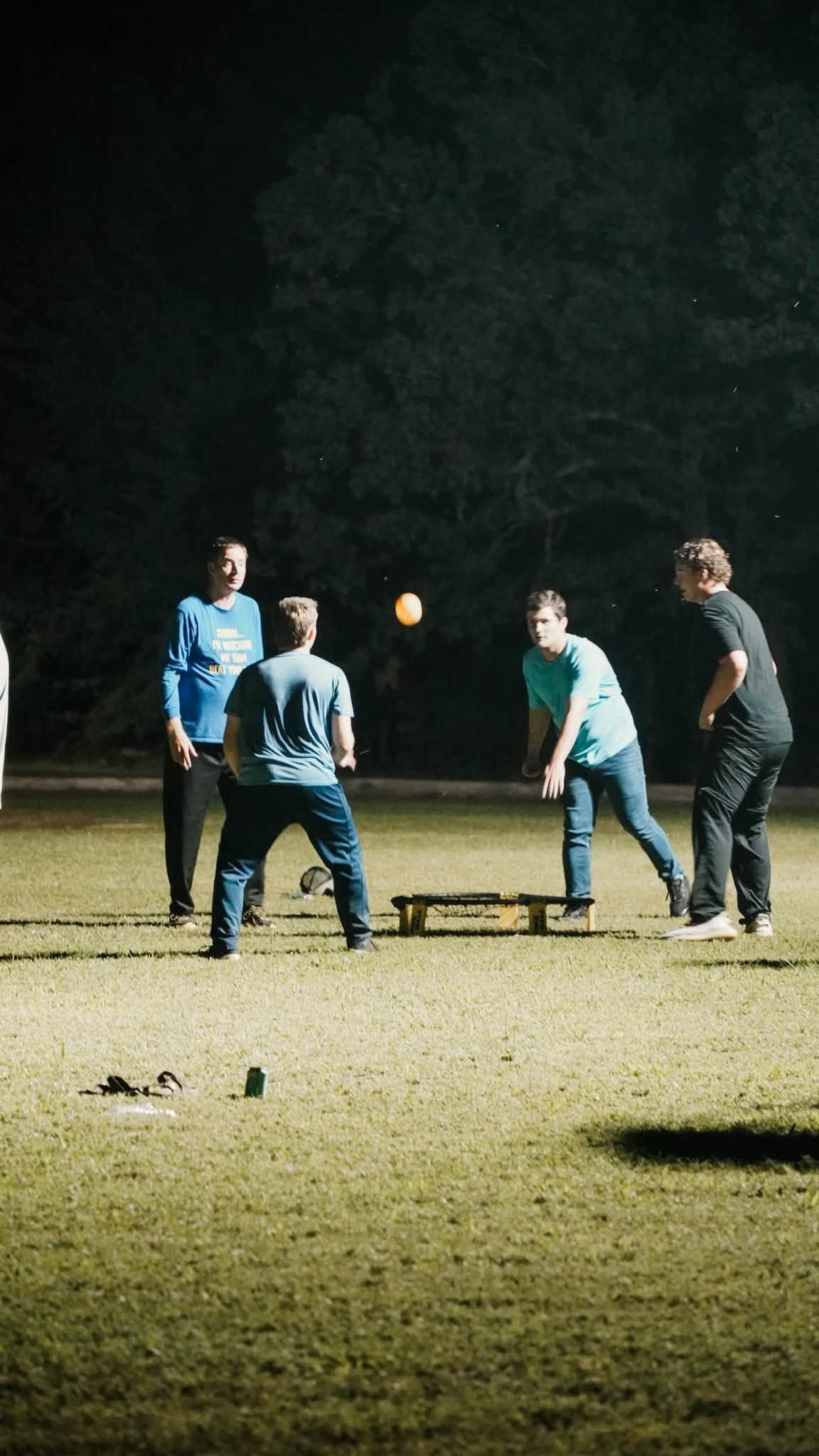 Four people stand on a lit grassy field at night, playing catch with a glowing ball.
