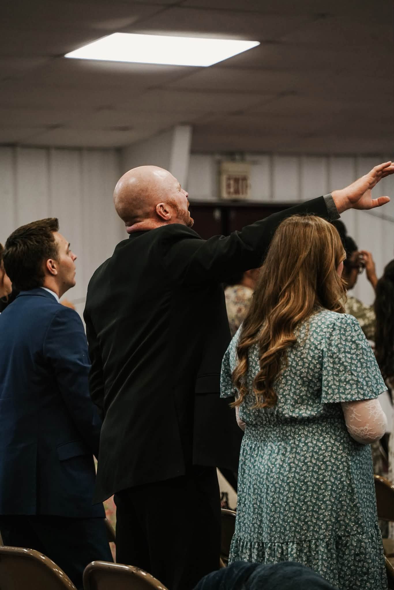 People standing indoors at a gathering, one person raising an arm while facing the front.