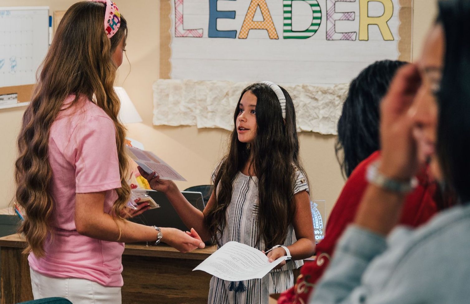 Two girls are standing next to each other in front of a sign that says leader.