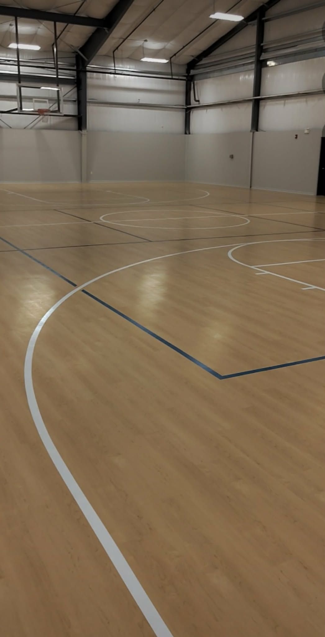 Empty indoor sports court with light wood flooring and white boundary lines under high ceiling lights