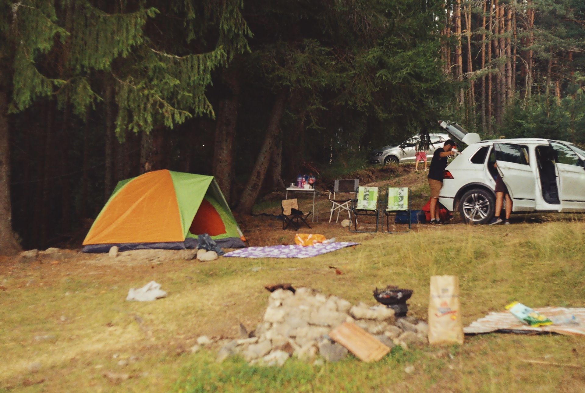 camping gear all over ground, and all car doors standing open, with folks still unloading