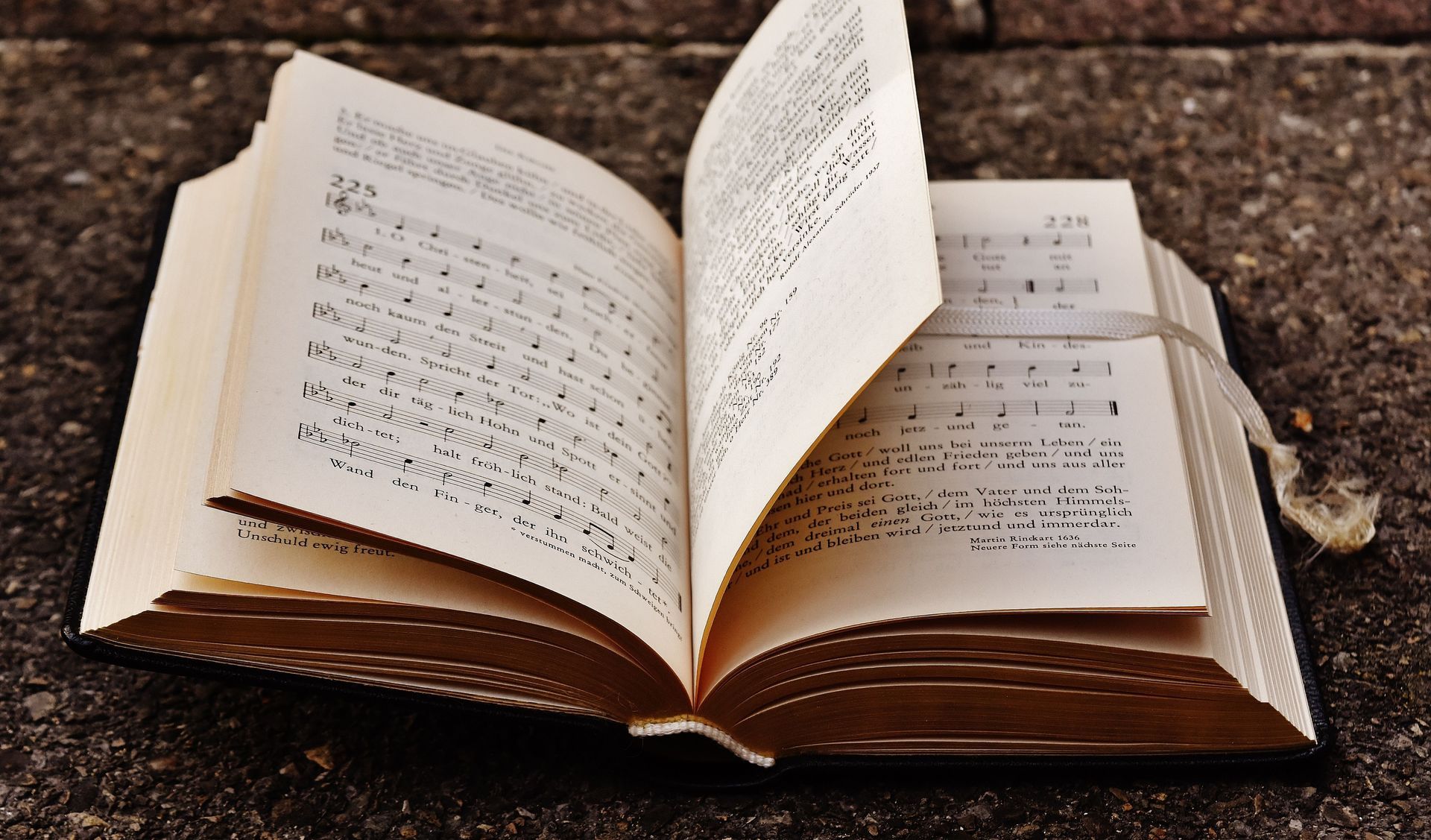 An open book with Arabic text resting on a surface outdoors.