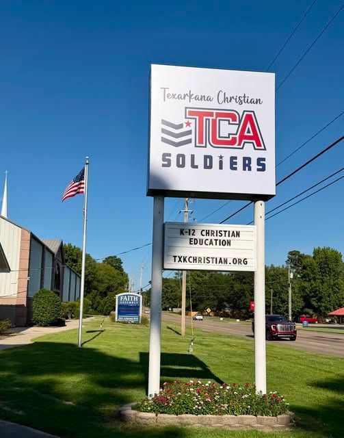 white sign of TCA soldiers on pole with church and flag in the background