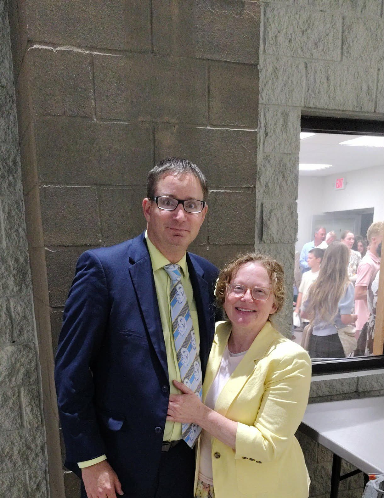 Two people posing indoors, dressed in blue and yellow, standing by a window at an event.
