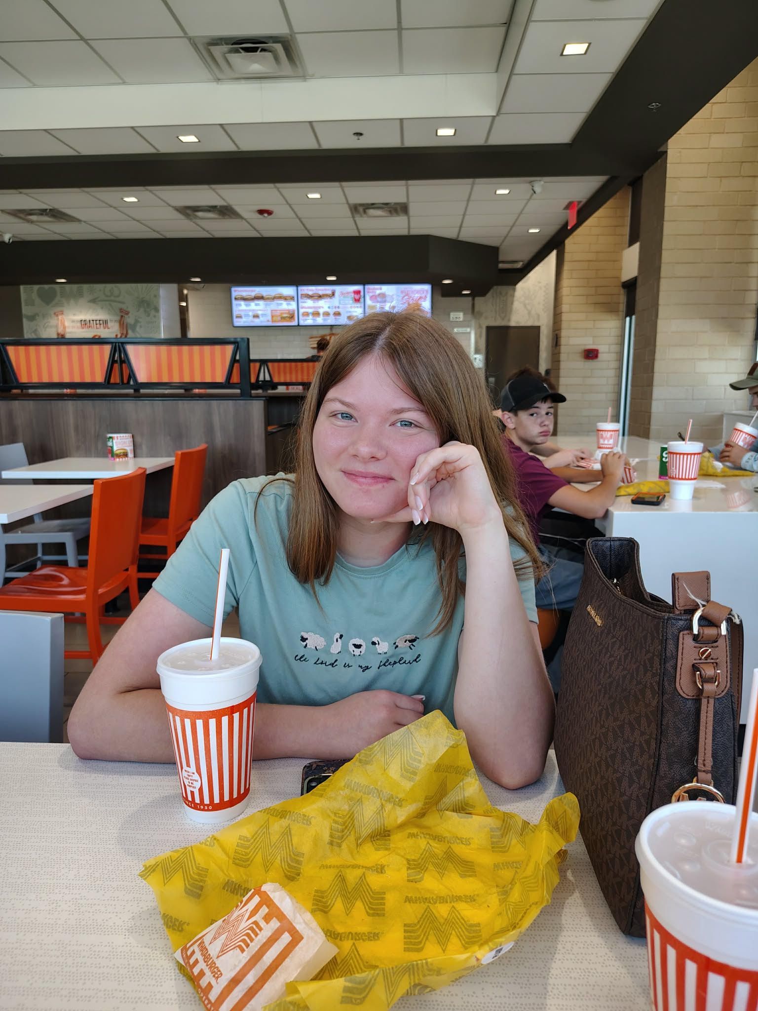 Woman sitting at a restaurant table with food and drinks, smiling at the camera.