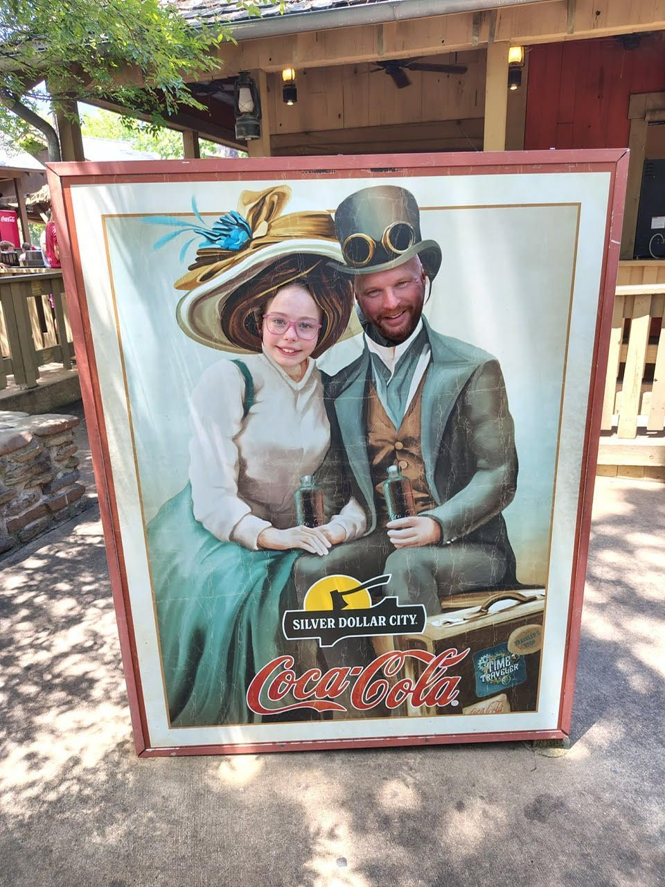 Coca-Cola stand-in board with a cutout of two vintage-style figures and a smiling face in the center