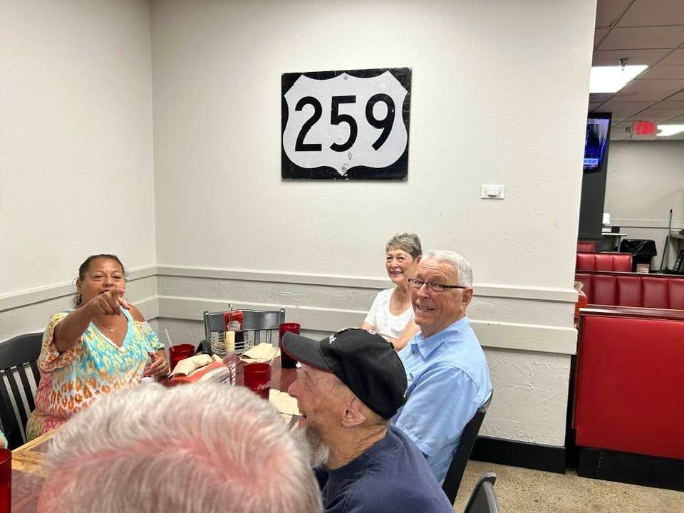 People seated at a table in a hall with a large “259” sign on the wall.