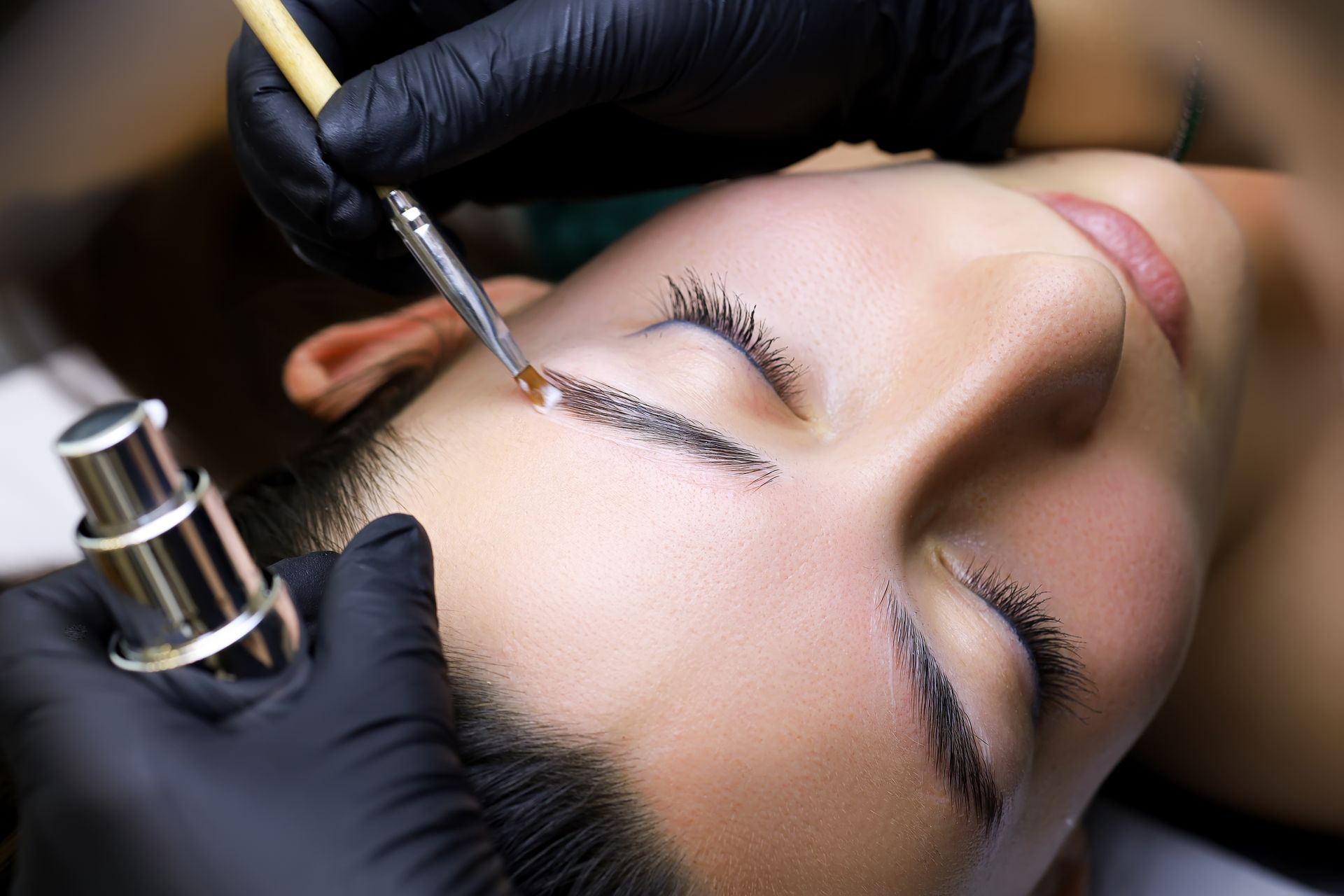 Microblading procedure on eyebrow and eyelid with gloved hands and cosmetic tool