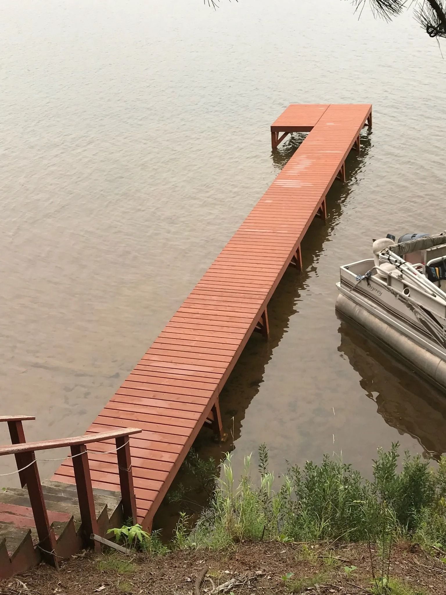 An orange dock with a patterned surface extends into a lake next to a boat, accessible by a short staircase.