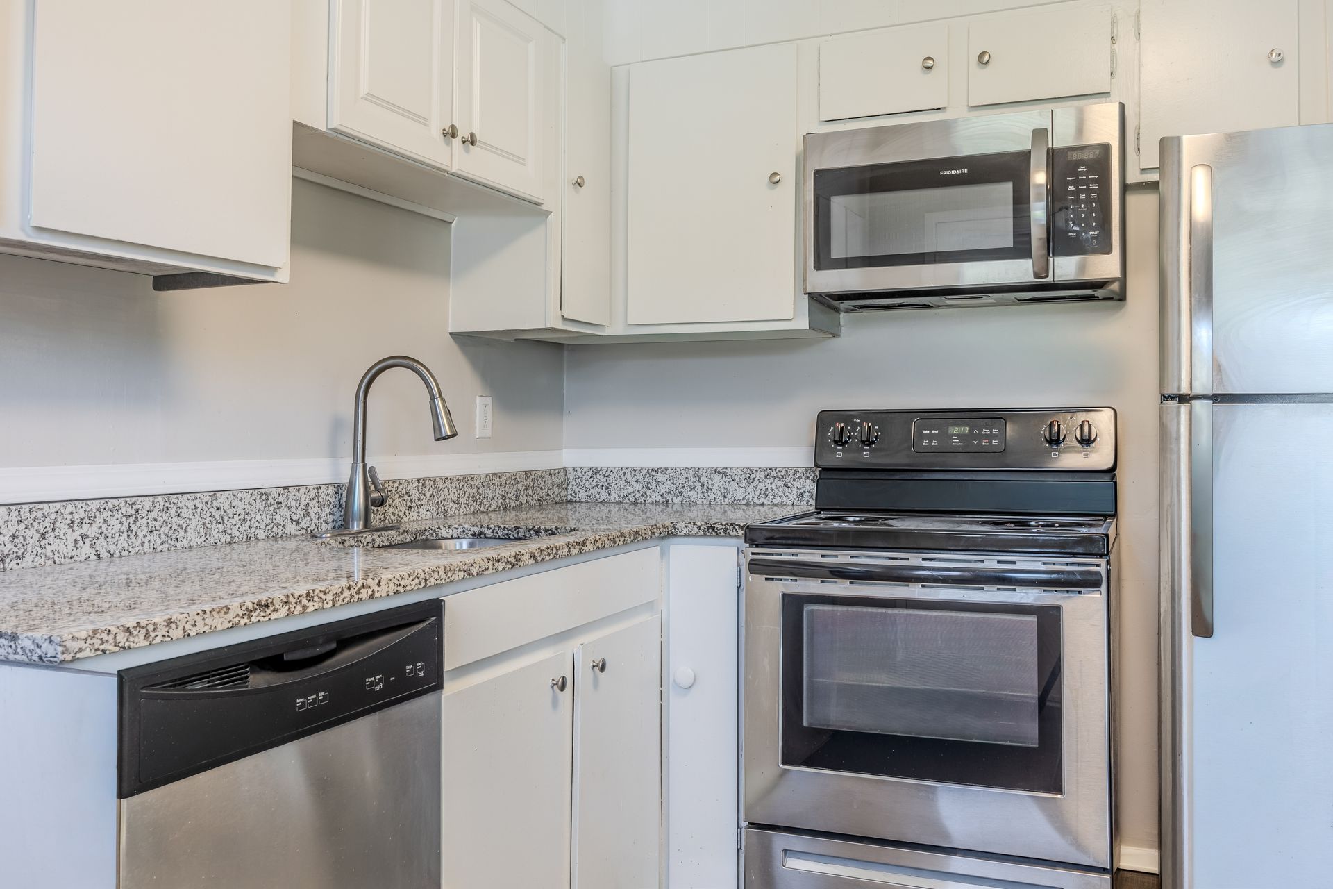 White kitchen with stainless steel appliances, cabinets, and light gray countertops.
