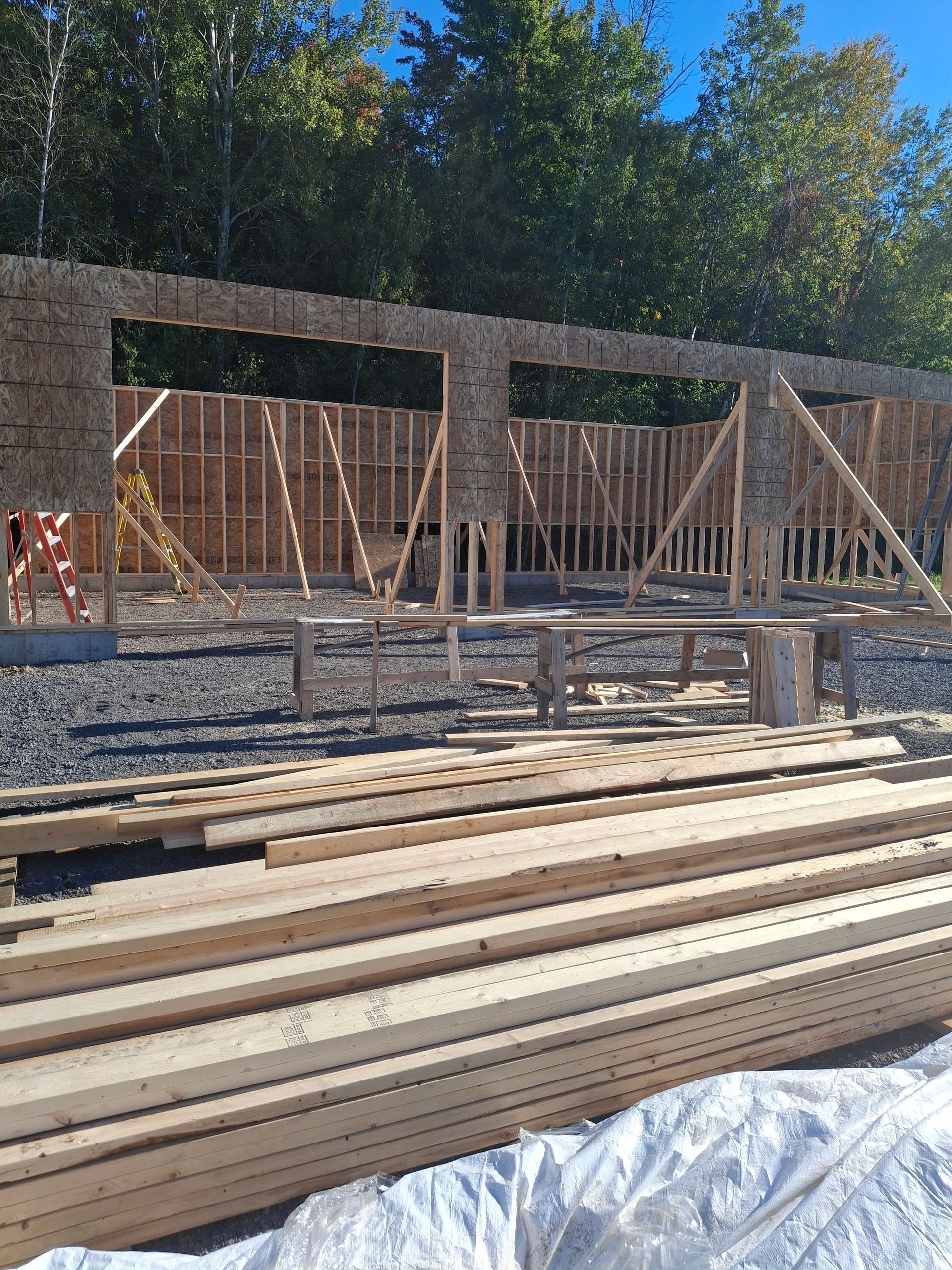 Construction site with wooden framing for a building. Stacked lumber in foreground, structure in progress, blue sky.