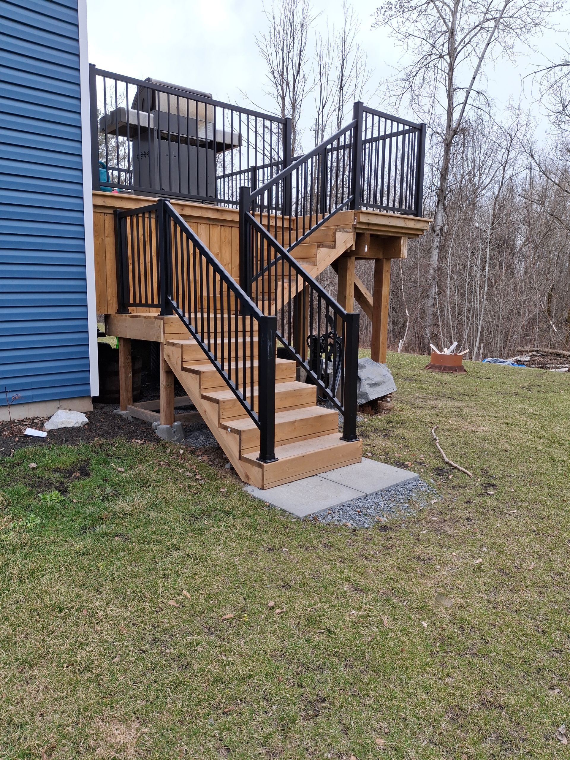 Wooden deck with black railing and stairs leading to a backyard.