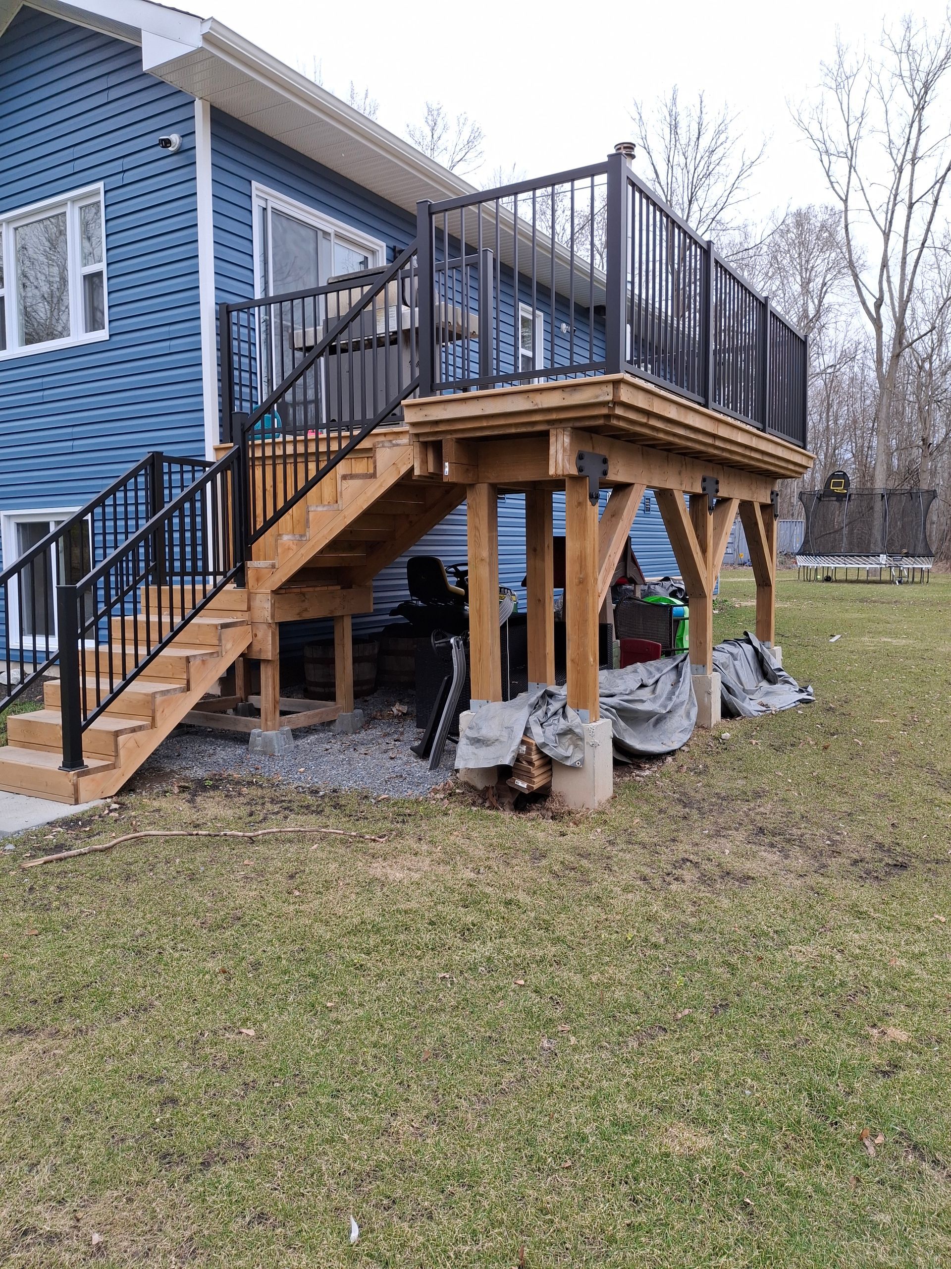 Blue house with wooden deck, black railings, and stairs leading to the yard.