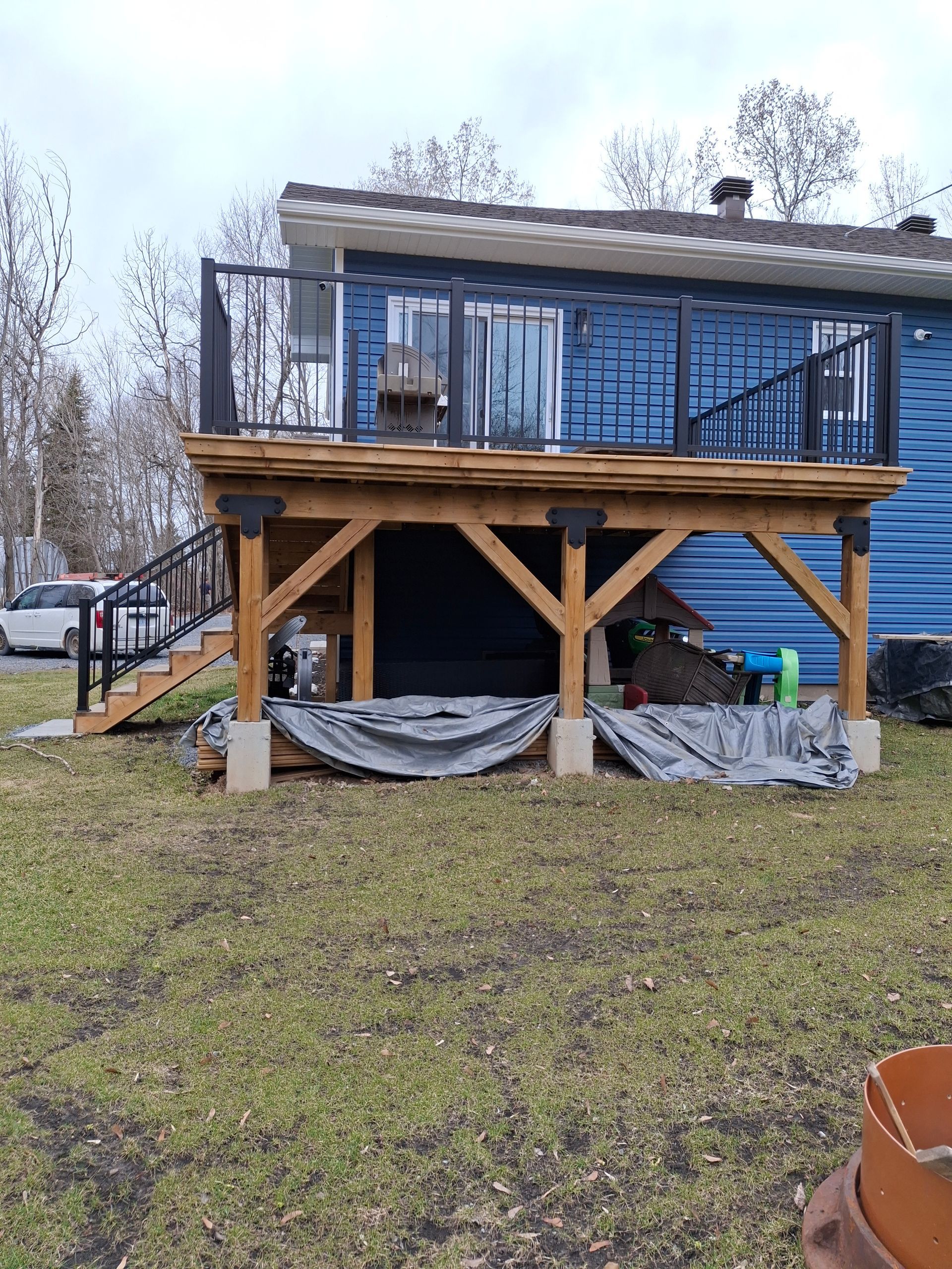 Wooden deck with black railings and stairs attached to a blue house on a grassy lawn.