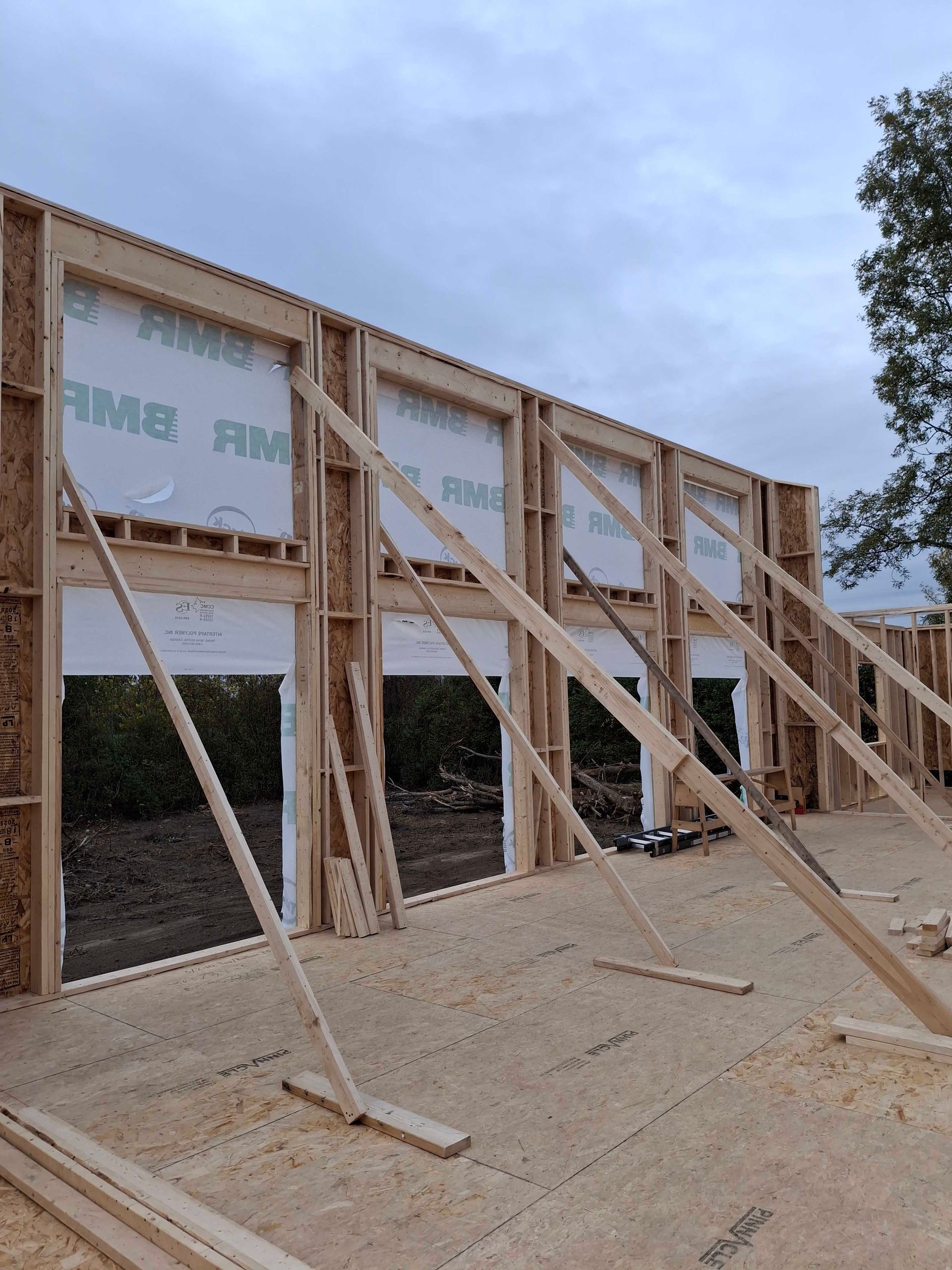 Wooden wall under construction, braced with diagonal supports. Cloudy sky in the background.