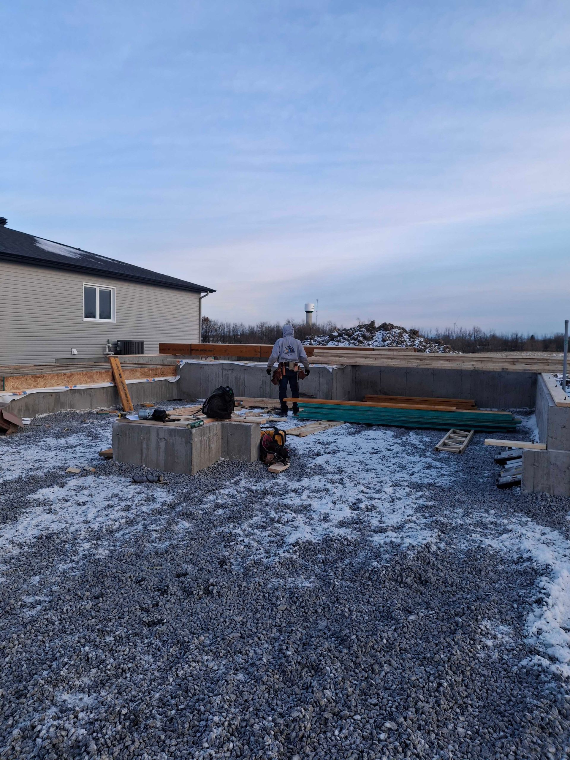 Construction worker on a new building foundation, gravel ground, partly cloudy sky.