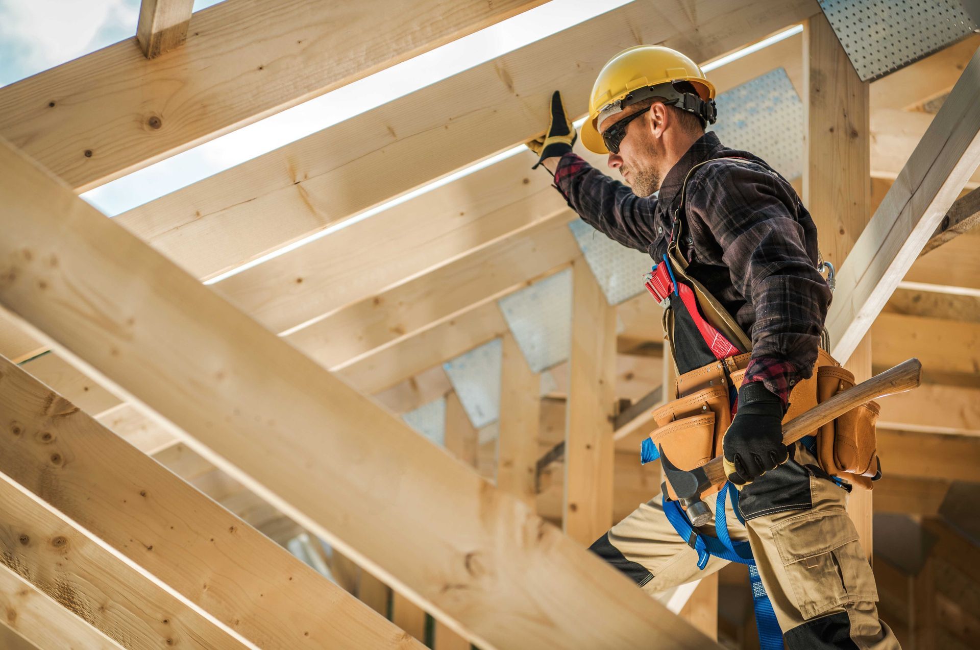 Construction worker on a wooden roof structure, wearing a hard hat and safety harness, checking the framework.