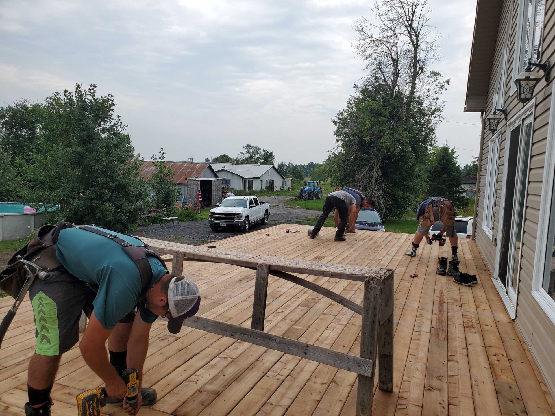 Three workers installing wooden deck boards on a sunny day.