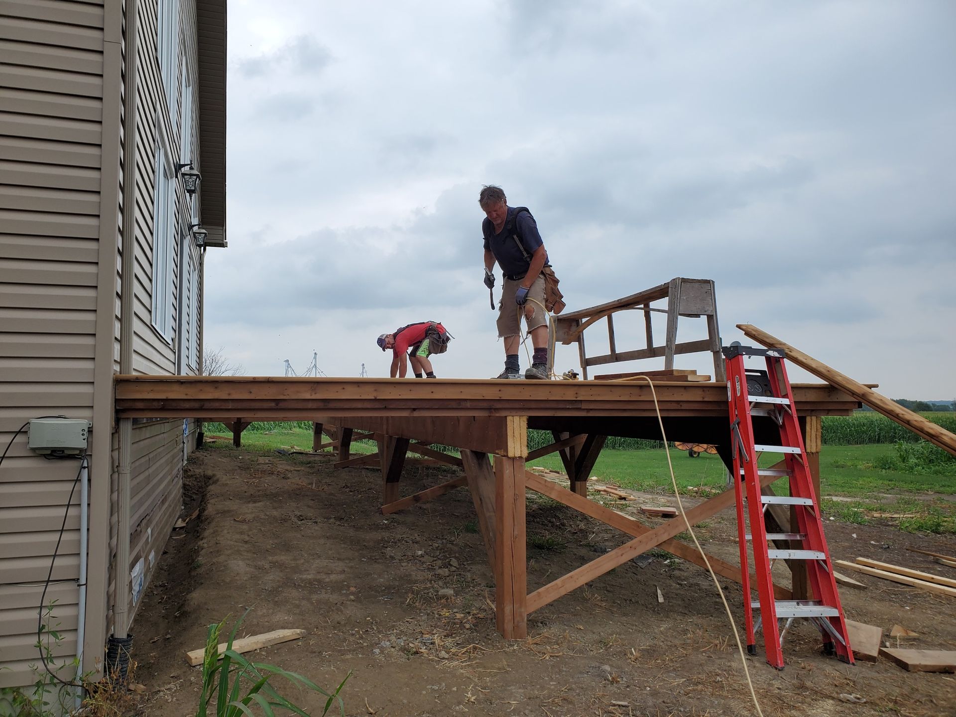 Two people building a wooden deck next to a house. One person is bending over while the other stands.