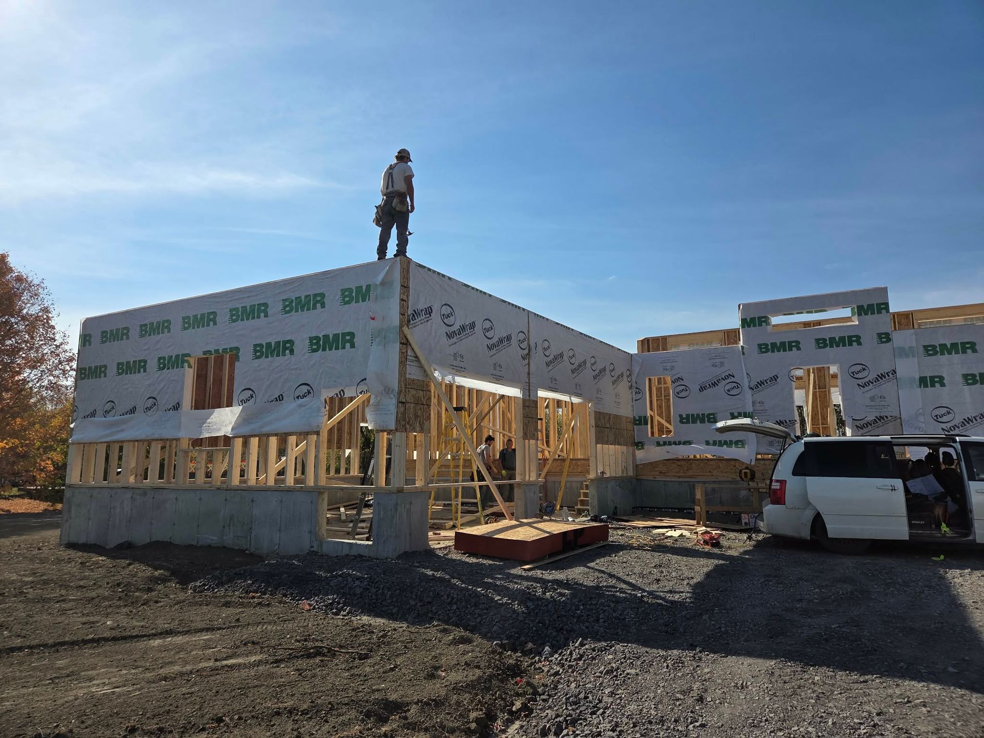 Construction site: A one-story building under construction with a worker on the roof on a sunny day.