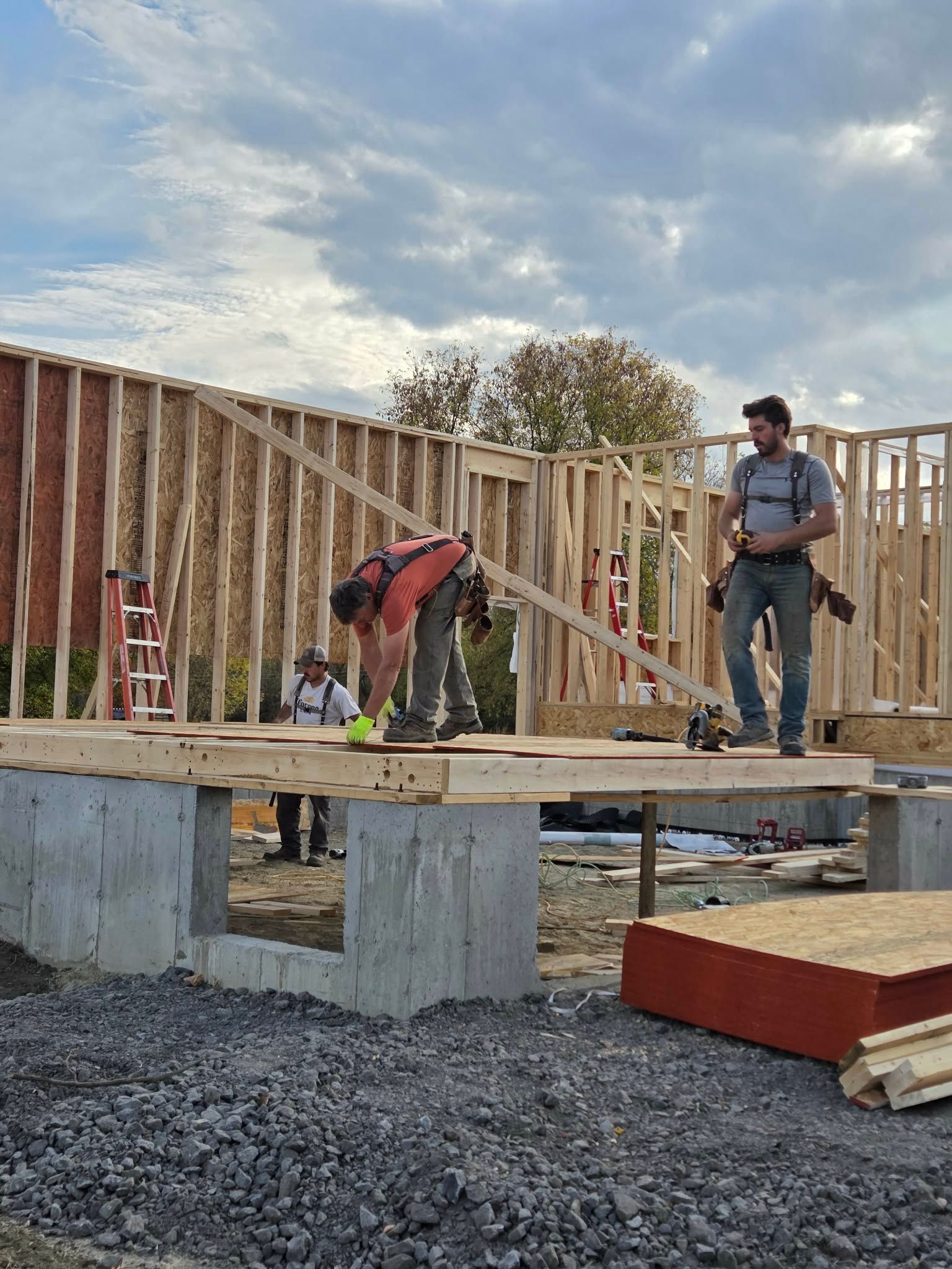 Construction workers building a wooden frame house on a concrete foundation under a cloudy sky.