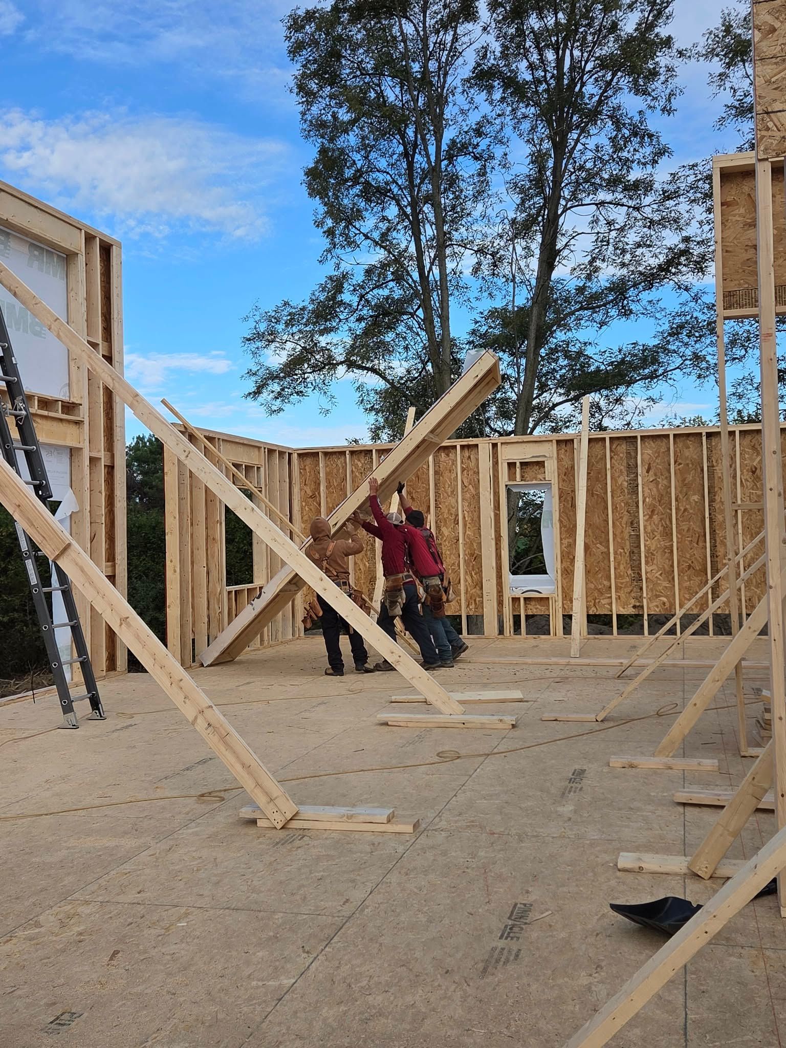 Two workers build wooden house frame under a blue sky.