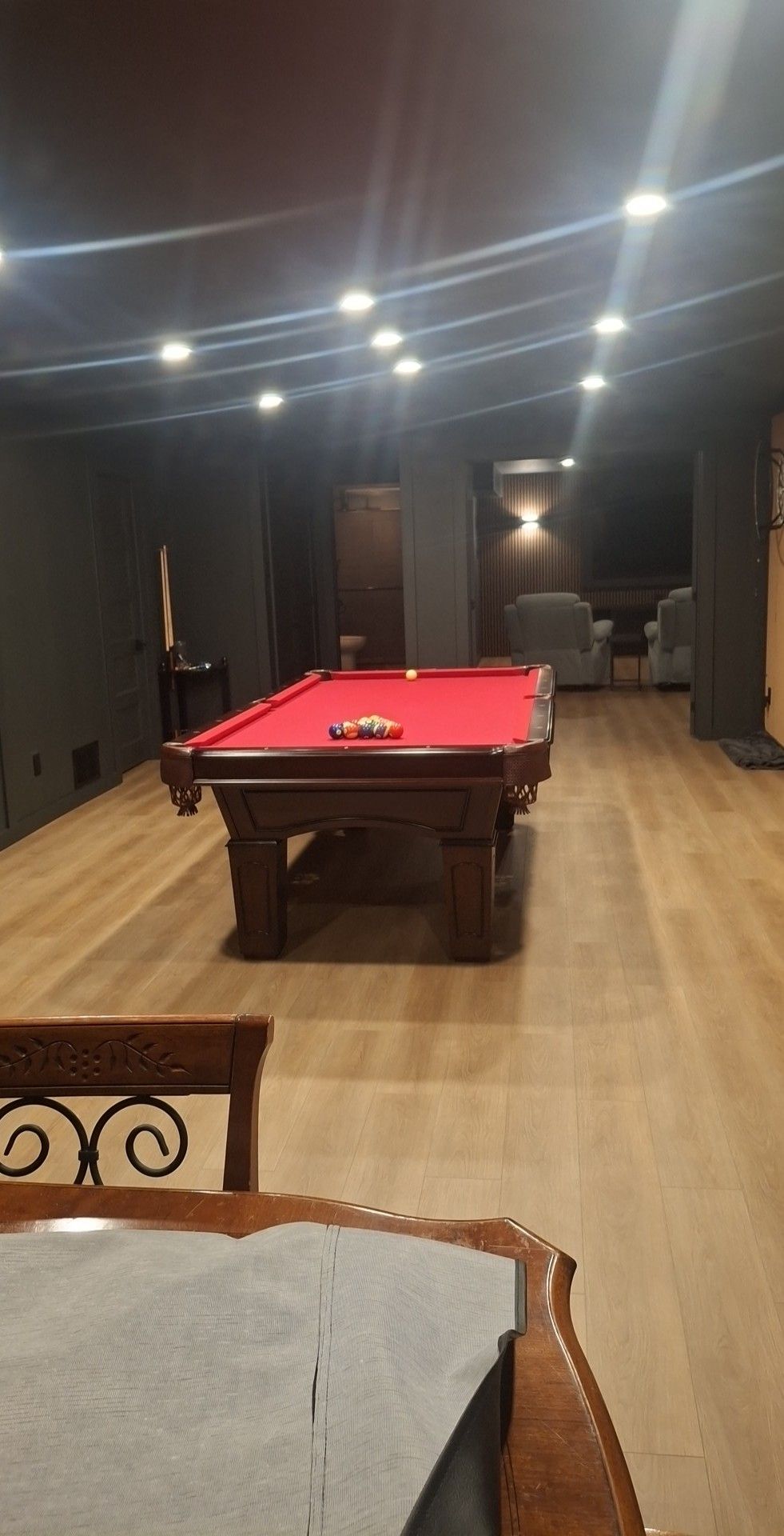 Pool table with red felt, in a dimly lit room with wood flooring.