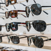 Rows of sunglasses displayed on shelves in a store, with dark tinted lenses and various frame styles