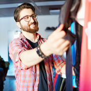 Bearded man in glasses hanging clothes on a rack in a brightly lit store
