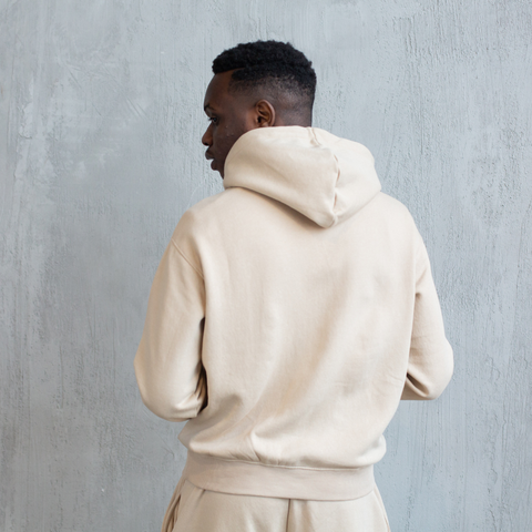 Person in a cream hoodie and matching pants, seen from behind against a gray wall.