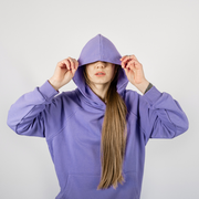 Person in a purple hoodie pulling the hood over their face against a plain gray background