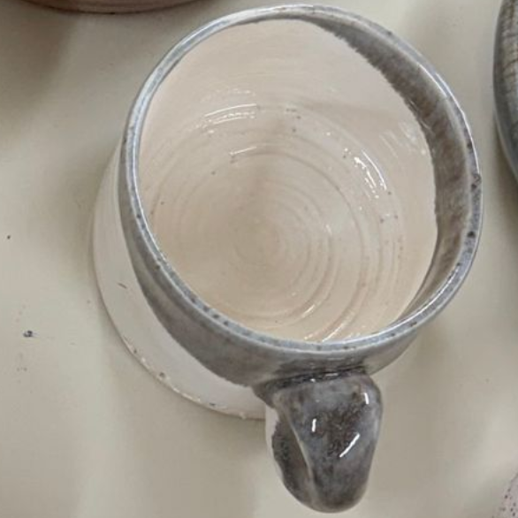 Top view of a white ceramic mug with a gray rim and handle, sitting on a light countertop