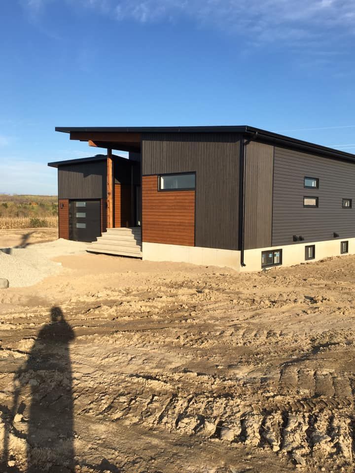 Maison moderne brun foncé sur un terrain sablonneux sous un ciel bleu clair