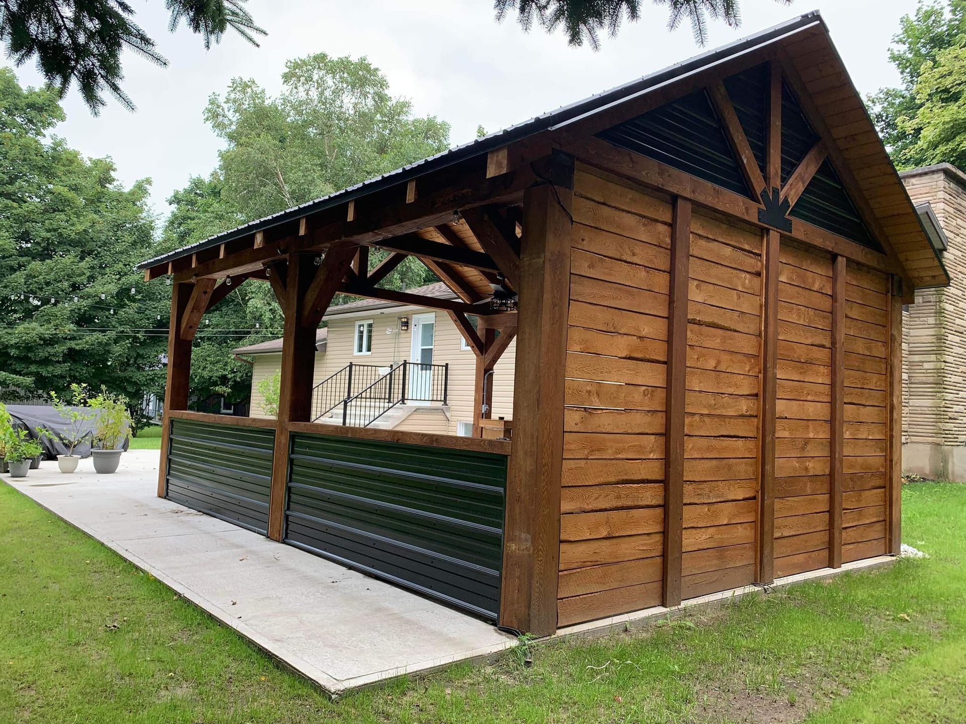 Abri de jardin extérieur en bois, ouvert sur les côtés et doté d'un toit en pente, situé à côté d'un chemin pavé sur la pelouse.