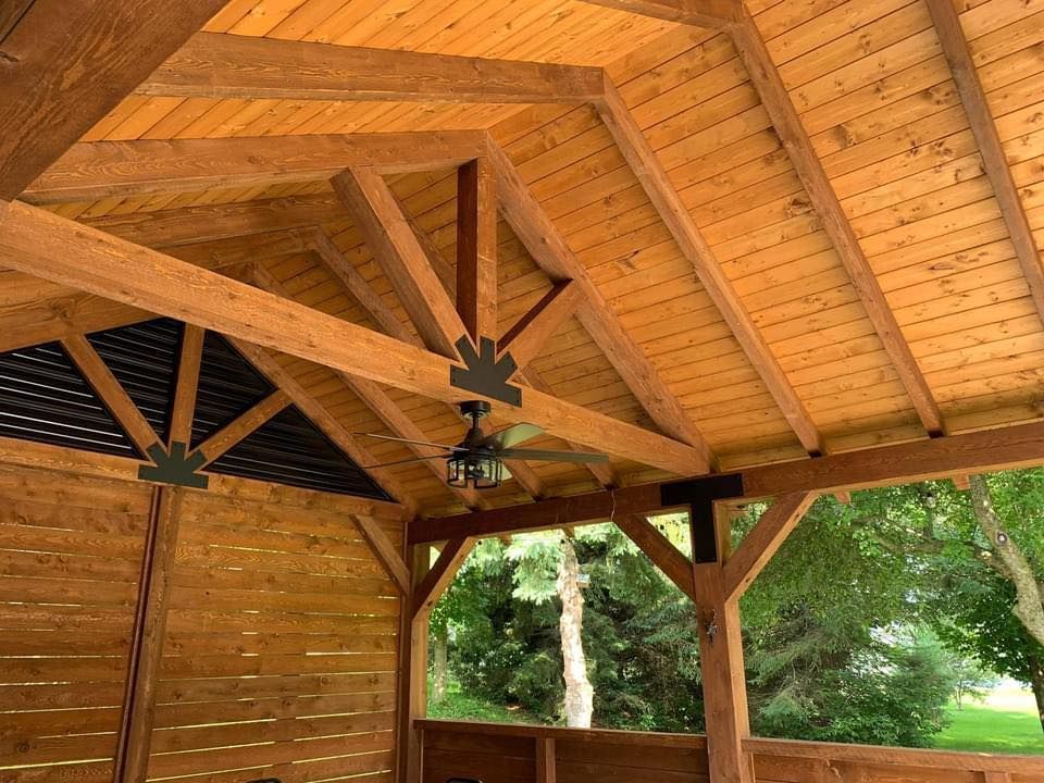 Pavillon avec plafond en bois, poutres apparentes et ventilateurs au-dessus d'un espace extérieur gazonné