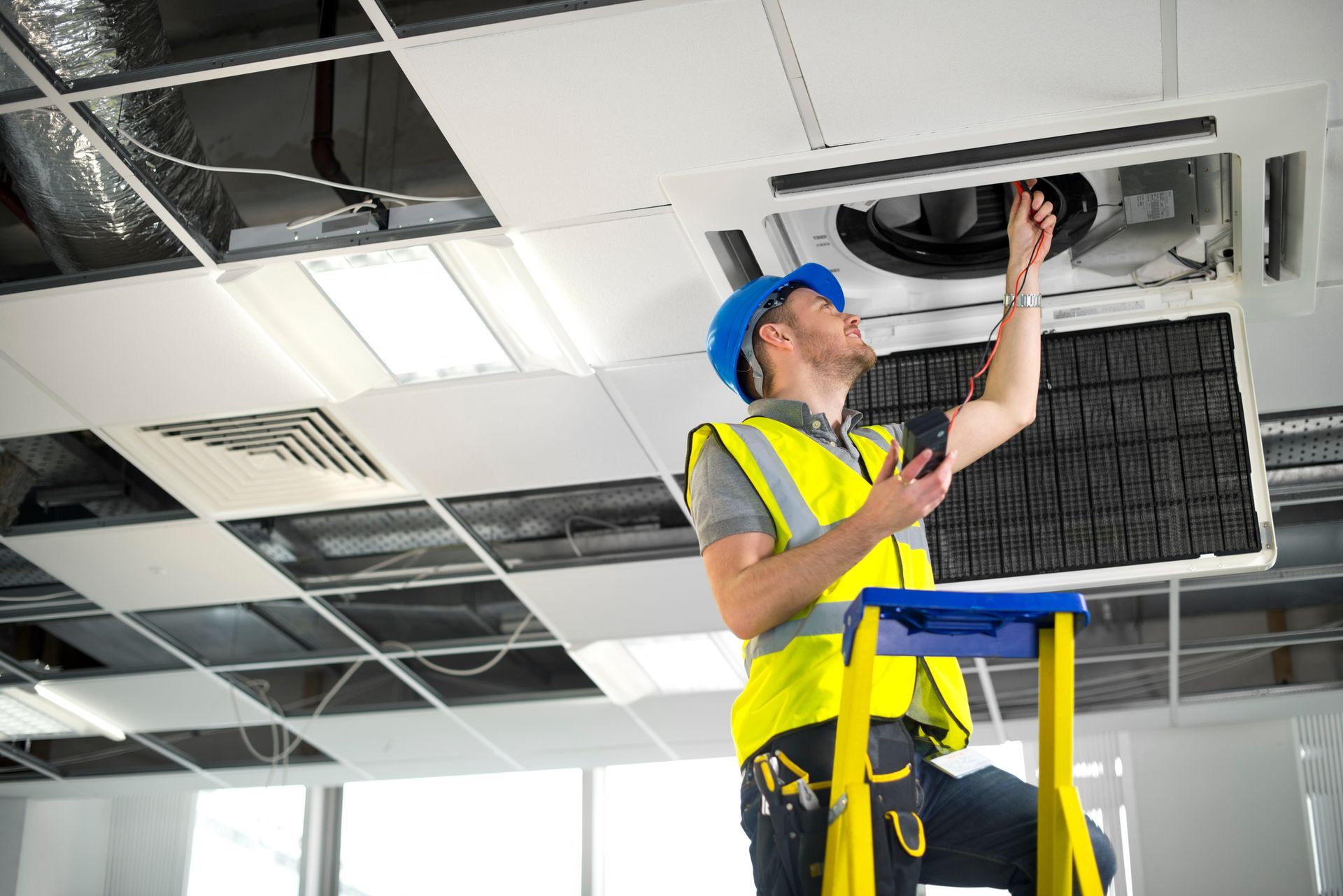 A man is standing on a ladder working on an air conditioner.
