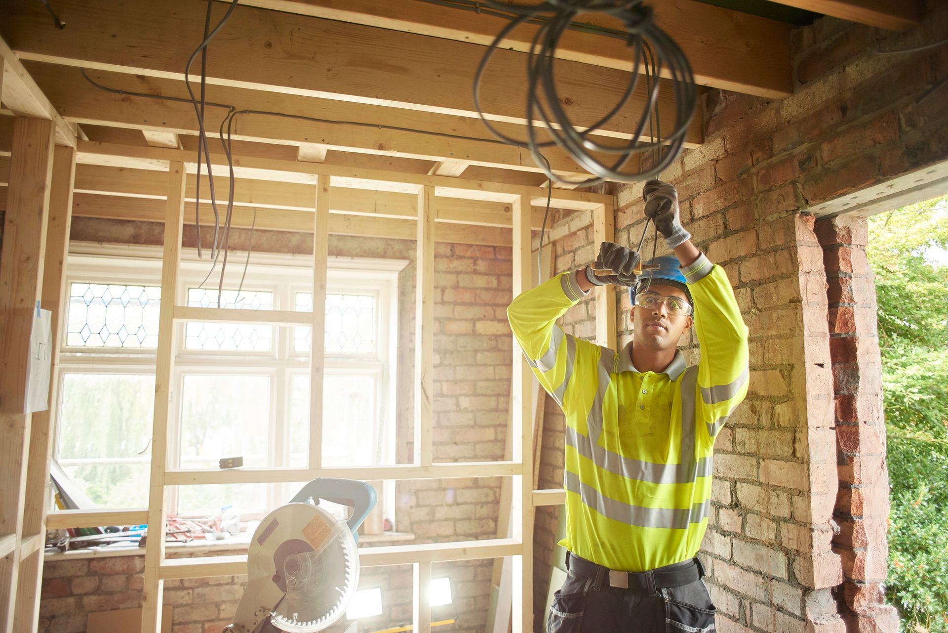 A man in a yellow safety vest is working on a ceiling