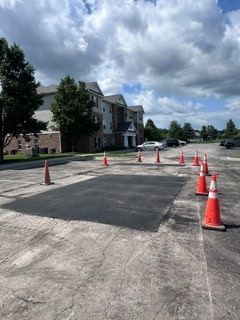 Roadwork area with orange cones marking a freshly patched asphalt section on a suburban street
