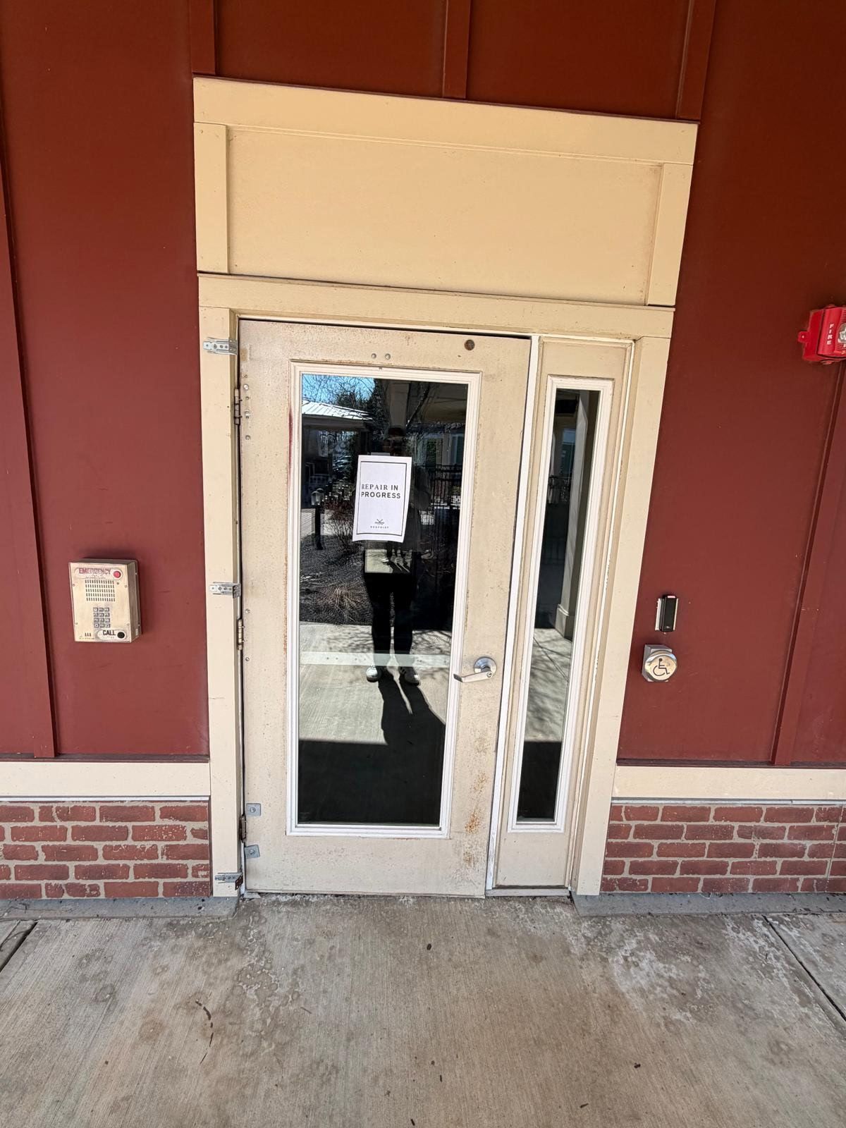 Glass storefront door with a paper notice, framed by red walls and brick at the base